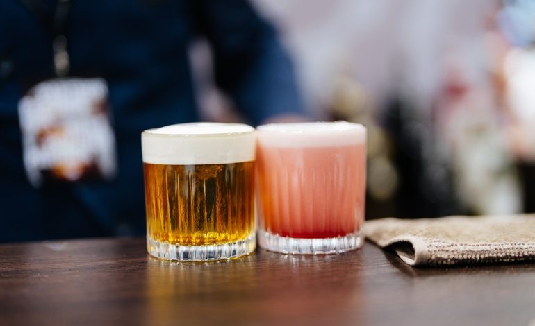 Two glasses of craft beer, one amber and one pink, sitting on a wooden bar counter in a San Diego brewery, representing craft beer culture and financial balance.