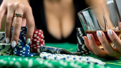 Close-up of a person holding a glass of beer and poker chips at a casino table.