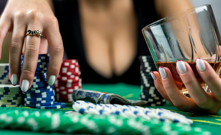 Close-up of a person holding a glass of beer and poker chips at a casino table.