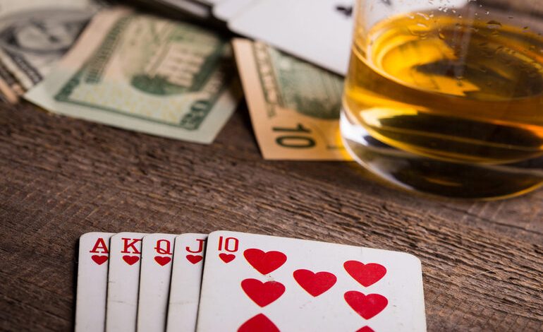 Royal flush in hearts with cash and beer on a wooden table, poker winning hand concept.