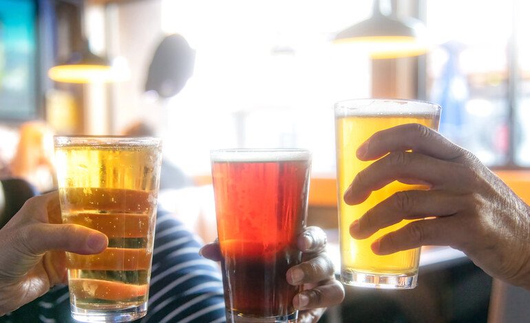 Three people clinking glasses of beer in a brewery taproom