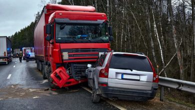 A red semi-truck is involved in a collision with a gray car on a highway.