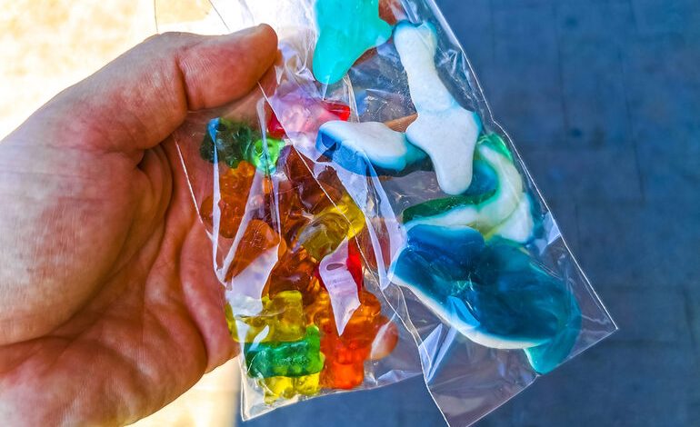 A person holding two clear plastic bags filled with colorful gummy candies, some shaped like bears and others like various animals.