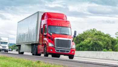 A red semi-truck driving on a highway under cloudy skies, representing legal driving limits for truckers and insights from Sarasota truck accident attorneys.