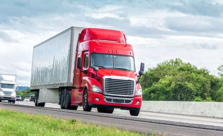 A red semi-truck driving on a highway under cloudy skies, representing legal driving limits for truckers and insights from Sarasota truck accident attorneys.