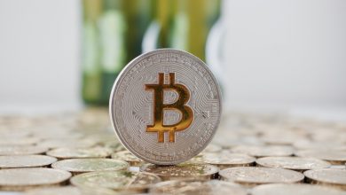 A coin of Bitcoin on a group of coins in front of a set of beer bottles.
