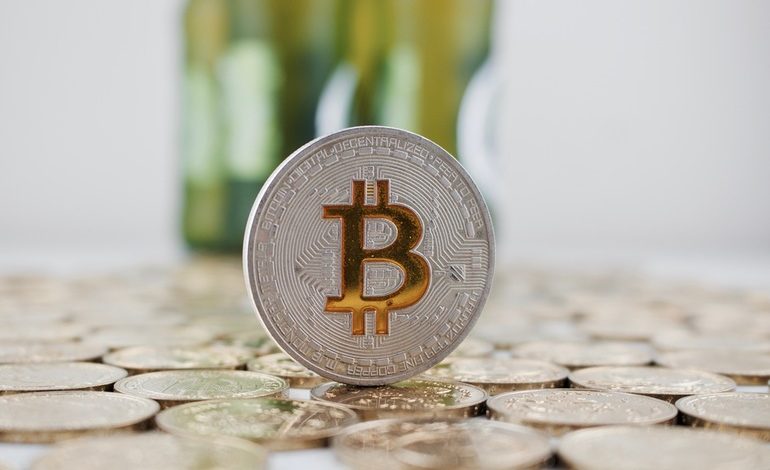 A coin of Bitcoin on a group of coins in front of a set of beer bottles.