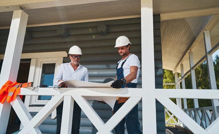 During a safety check of a residential deck, the construction inspectors in hard hats examine the building plans of the deck.
