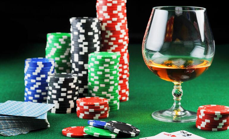 Glass of craft beer beside stacked casino chips and playing cards on a green gaming table, representing casino gaming strategies.