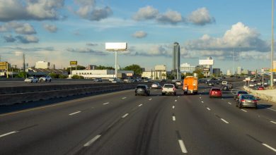 Wide highway with multiple lanes, cars, and an HOV lane during daytime under a partly cloudy sky.