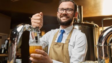 Smiling brewery worker in an apron pouring draft beer from a tap, illustrating an independent contractor role at a brewery.