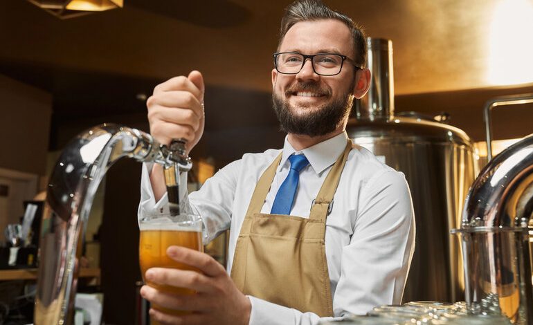 Smiling brewery worker in an apron pouring draft beer from a tap, illustrating an independent contractor role at a brewery.