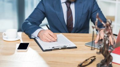 A lawyer is writing a legal contract while looking at a laptop.