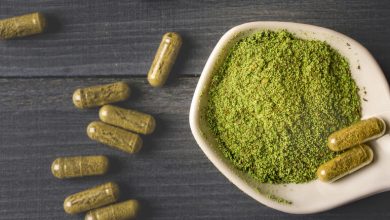 Green Dragon Kratom powder in a small bowl with kratom capsules scattered on a dark surface.