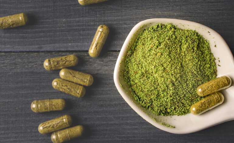 Green Dragon Kratom powder in a small bowl with kratom capsules scattered on a dark surface.