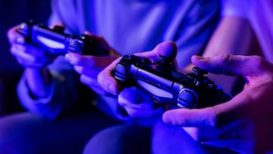 Two people holding video game controllers while playing together under blue ambient lighting.