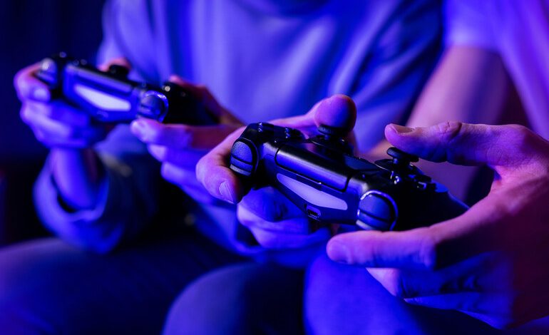 Two people holding video game controllers while playing together under blue ambient lighting.