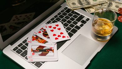Laptop with playing cards, and a drink on a gaming table, capturing a relaxed gaming night atmosphere.
