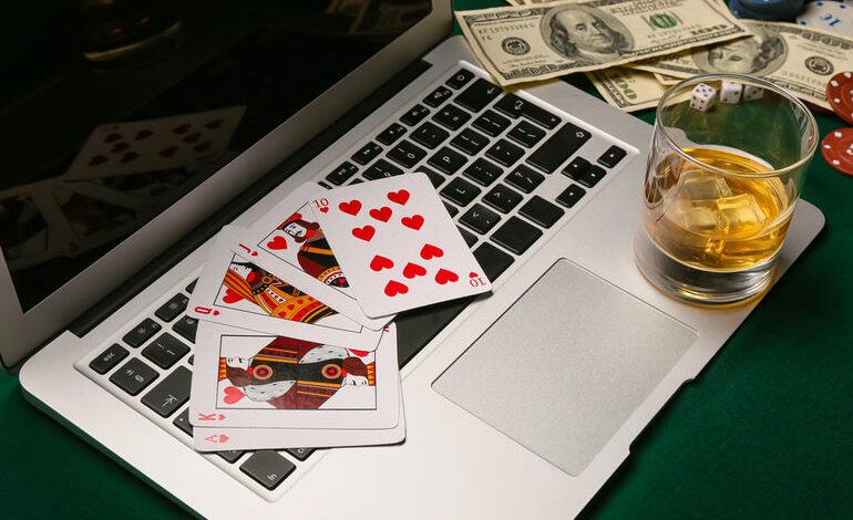 Laptop with playing cards, and a drink on a gaming table, capturing a relaxed gaming night atmosphere.
