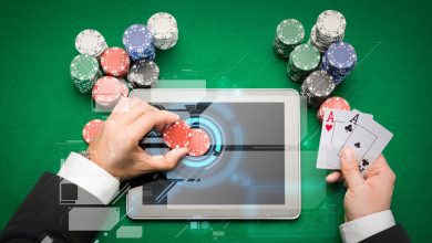 A gambler is playing online casino games on a digital tablet with poker chips and cards in hand.