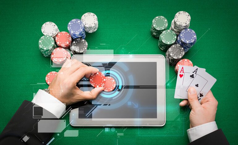 A gambler is playing online casino games on a digital tablet with poker chips and cards in hand.