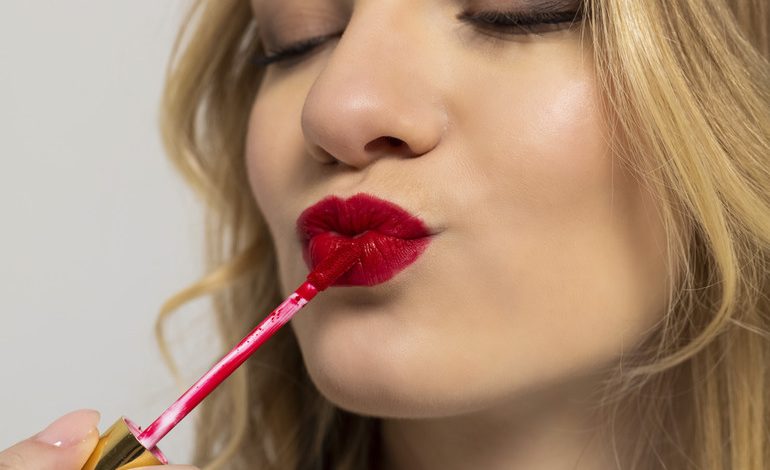 Woman applying red liquid lipstick with a wand, showing smooth coverage designed to stay comfortable through long nights and late beer runs.
