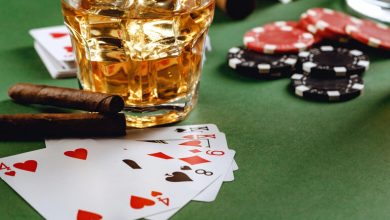 Glass of beer with poker cards, casino chips, and cigars on a green table at an online casino setting.