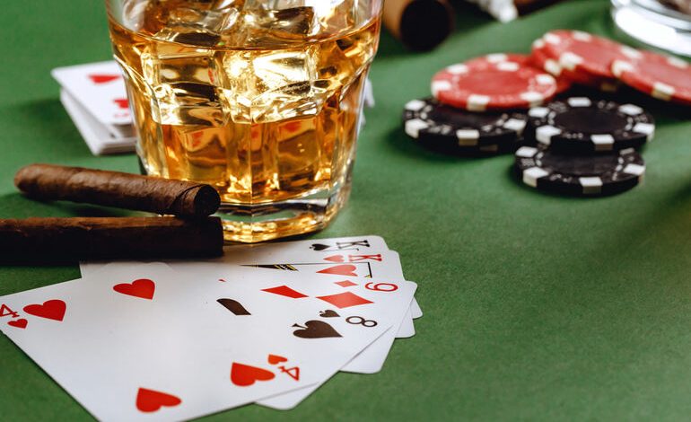 Glass of beer with poker cards, casino chips, and cigars on a green table at an online casino setting.
