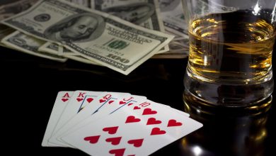 A cold glass of alcohol next to a credit card and playing cards on a casino table.