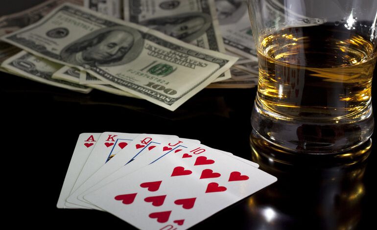 A cold glass of alcohol next to a credit card and playing cards on a casino table.