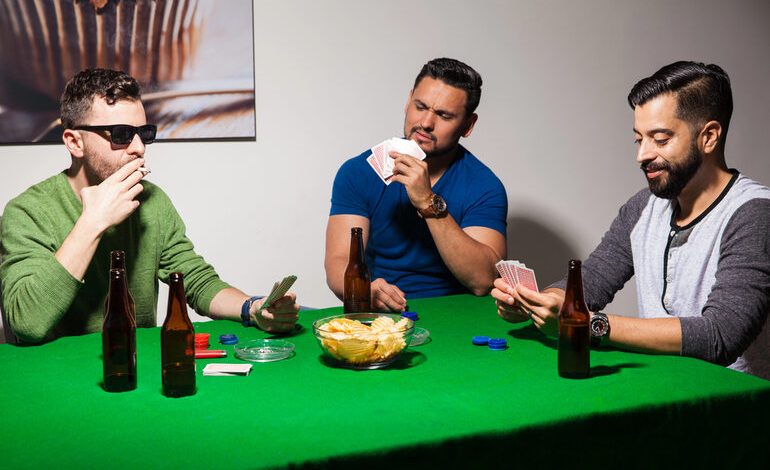 Friends at home playing poker around a green table with cards and chips, as well as bottles of beer, during a low-key casino night.