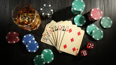 Poker cards, casino chips, dice, and a glass of alcohol on a dark table, which depicts the connection between gambling and drinking alcohol.