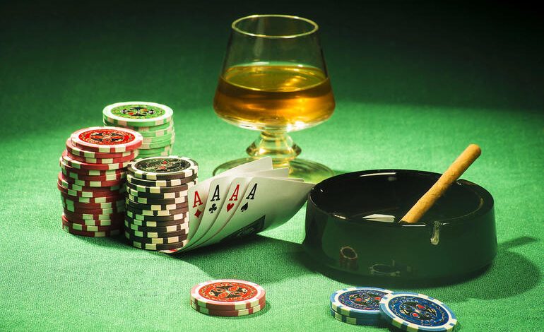 Glass of craft beer with poker chips, playing cards, and a cigar on a casino table.