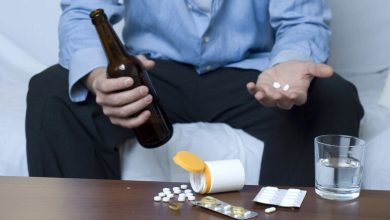 Man holding a beer bottle and pills, showing early signs of beer addiction and substance misuse