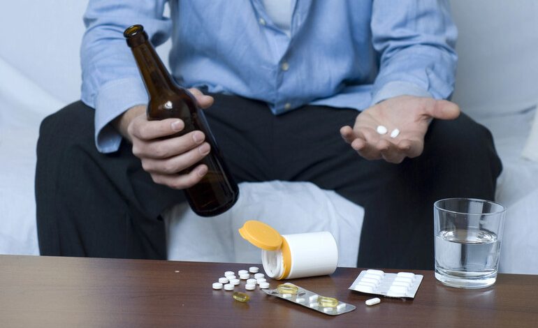 Man holding a beer bottle and pills, showing early signs of beer addiction and substance misuse