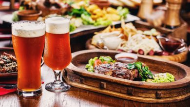 Two glasses of amber craft beer served alongside a steak dinner with fries, salad, and dipping sauces, representing craft beer choices for a San Diego wedding dinner menu.
