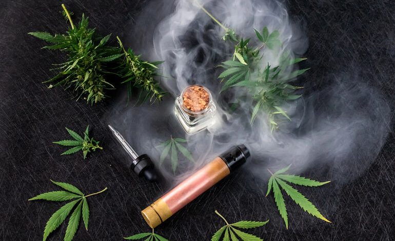 Flat lay of THC vape pen with cannabis leaves and vapor.