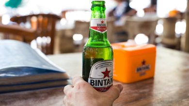 Hand holding a cold bottle of Bintang beer on a wooden table in an Indonesian café.