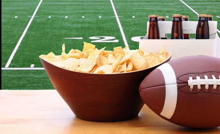 Chips, American football, and Six Pack of Beer on the table.