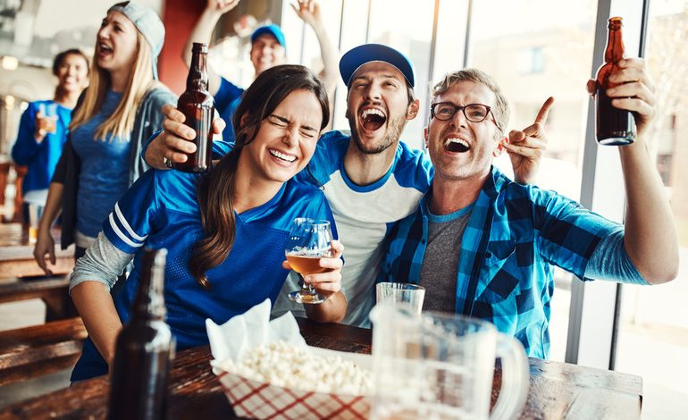 Football fans celebrating a game-day win while drinking beer at home, showing how sports sponsorships connect betting, live matches, and beer-loving audiences.