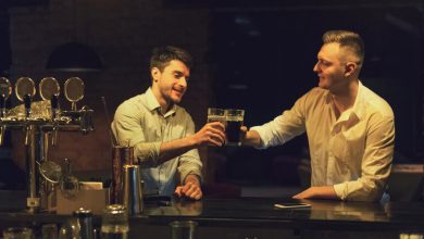 Two friends clinking glasses of beer while chatting at a cozy bar counter in the evening.