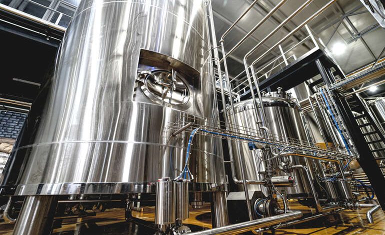 Stainless steel fermentation tanks and piping inside a modern craft brewery facility.