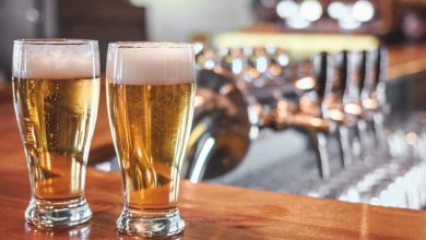 Two golden craft beers on a bar counter with taps in the background.
