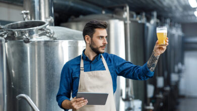 Brewer using a digital tablet to inspect craft beer quality inside a modern brewery.