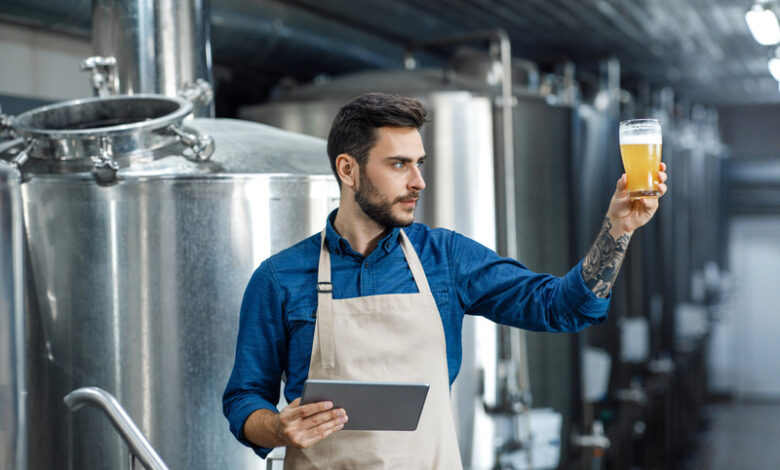 Brewer using a digital tablet to inspect craft beer quality inside a modern brewery.
